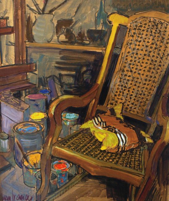 La mecedora del estudio Silla de mimbre con un cojín amarillo, rodeada de latas de pintura y objetos variados.